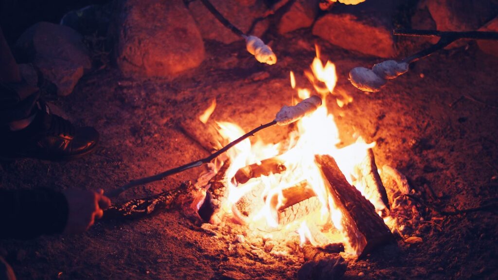 A warm campfire at night with marshmallows roasting on sticks, creating a cozy outdoor setting.