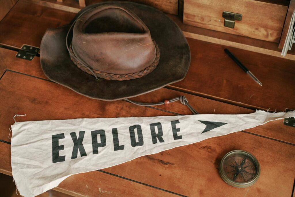 Vintage explorer's setup with a compass, hat, and 'Explore' banner on a wooden desk.